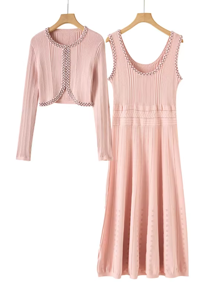 A two-piece women's outfit set in dusty pink, featuring a long-sleeve cropped cardigan and a matching sleeveless midi dress, both hanging on wooden hangers against a plain white background.