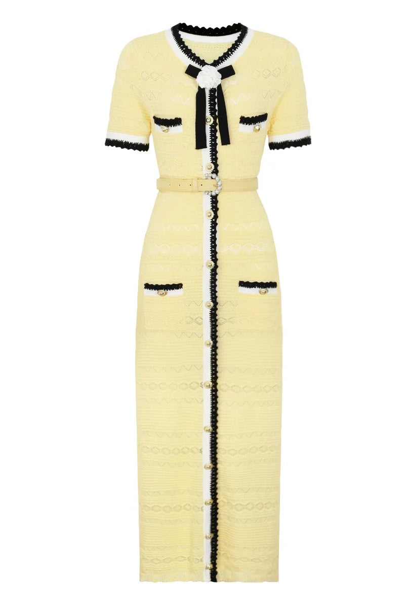 A pale yellow tweed midi dress with black and white trim, featuring a short-sleeve design, a black bow at the collar, a matching waist belt, and decorative buttons down the front.