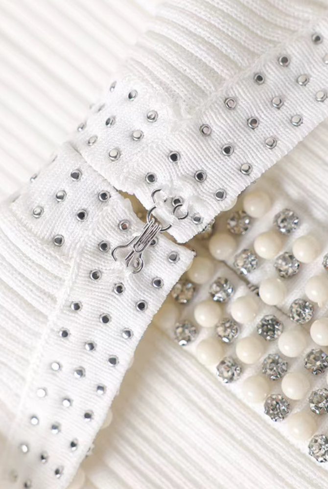 Close-up of a white pleated fabric accessory with silver rhinestone studs and a row of cream-colored rhinestone beads.