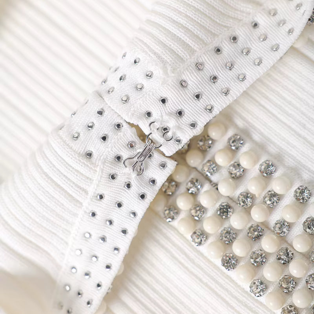 Close-up of a white pleated fabric accessory with silver rhinestone studs and a row of cream-colored rhinestone beads.
