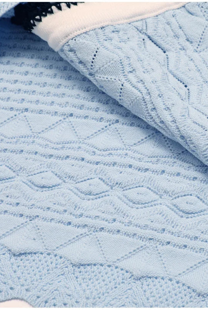 A light blue cable-knit blanket with textured diamond and waffle patterns, draped to show its soft folds and knit details.