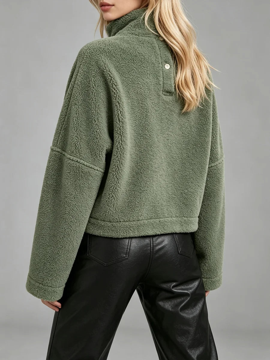 A woman wearing an olive green sherpa fleece mock neck pullover with a buttoned collar detail, paired with black leather pants, shown from a rear three-quarter angle against a neutral gray studio background.