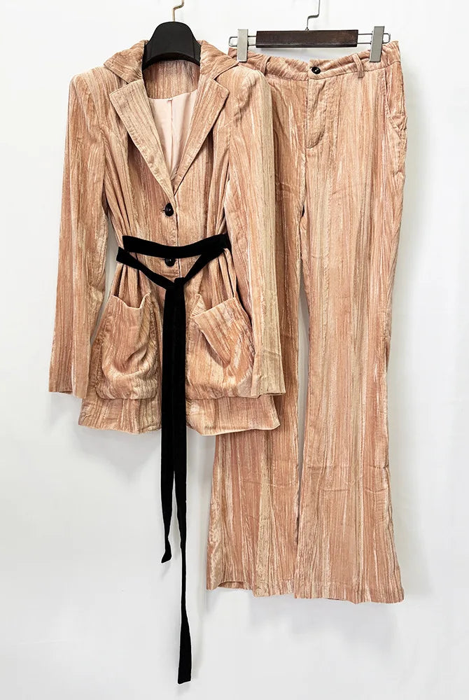 A two-piece women's outfit set featuring a long-sleeve belted blazer and matching wide-leg trousers in a textured, vertically striped peach-beige corduroy-like fabric, styled with a black velvet tie belt, hanging on black hangers against a plain white wall.