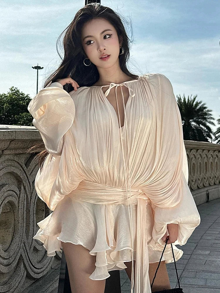 Woman wearing a cream ruched long sleeve mini dress with tie neckline and ruffle hem