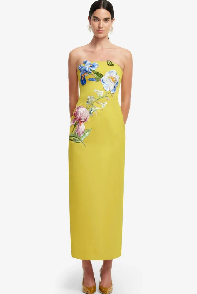 A woman modeling a strapless yellow maxi dress with colorful floral embroidery on the bodice and side.