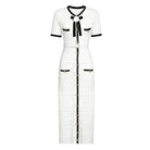 A white tweed midi dress with black trim and gold-tone accents, featuring short sleeves, a black bow at the collar, and a front button closure.