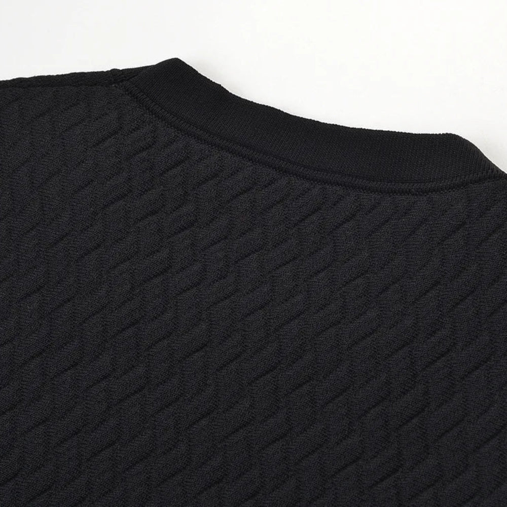Close-up of a black textured knit top showing the crew neck collar and diamond-patterned fabric against a plain white background.