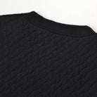 Close-up of a black textured knit top showing the crew neck collar and diamond-patterned fabric against a plain white background.