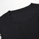 Close-up of a black textured knit top with a crew neck and scalloped sleeve edges, shown against a plain white background.