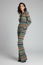 A model wearing a long-sleeve, V-neck knit outfit sets with a colorful chevron zigzag pattern in black, gray, yellow, blue, red, and white, standing against a neutral gray studio background.