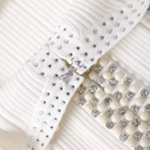 Close-up of a white pleated fabric accessory with silver rhinestone studs and a row of cream-colored rhinestone beads.