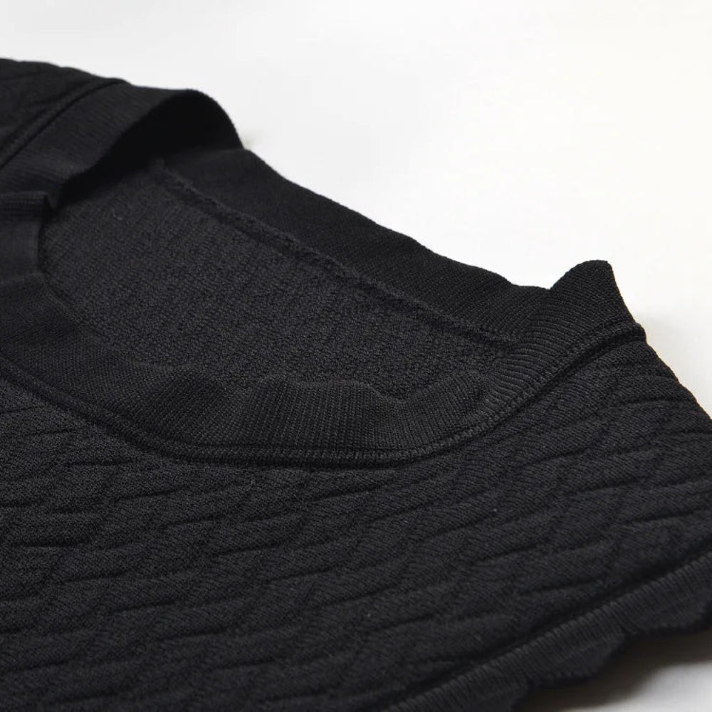 Close-up of a black textured knit garment, showing the ribbed crew neck collar and fine fabric weave on a white background.