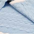 A light blue cable-knit blanket with textured diamond and waffle patterns, draped to show its soft folds and knit details.