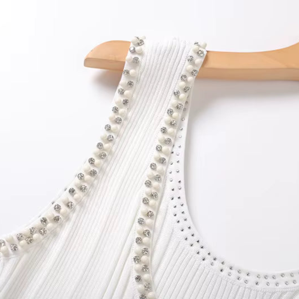 Close-up of a white ribbed dress with decorative straps featuring white pearls and silver rhinestones, hanging on a light wood hanger against a white background.