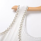 Close-up of a white ribbed dress with decorative straps featuring white pearls and silver rhinestones, hanging on a light wood hanger against a white background.