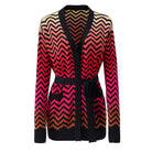 A women's long-sleeve knit cardigan with a V-neck and self-tie belt, featuring a bold chevron zigzag pattern in black, red, pink, and beige, shown against a plain white background.
