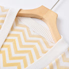 Close-up of a knit sweater with a yellow and white chevron pattern, draped over a light wood hanger against a white background.