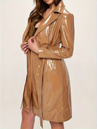 A woman wearing a shiny, glossy tan trench coat with a high collar and front zipper, shown against a plain light background.