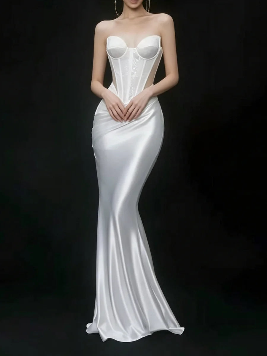 A strapless white satin gown with a structured corset-style bodice and a fitted mermaid silhouette, shown on a model against a dark studio background.