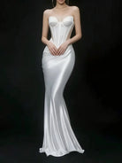 A strapless white satin gown with a structured corset-style bodice and a fitted mermaid silhouette, shown on a model against a dark studio background.
