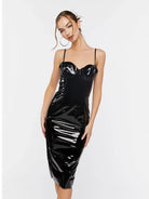 A woman modeling a black glossy faux-leather midi dress with spaghetti straps and a sweetheart neckline against a plain white studio background.