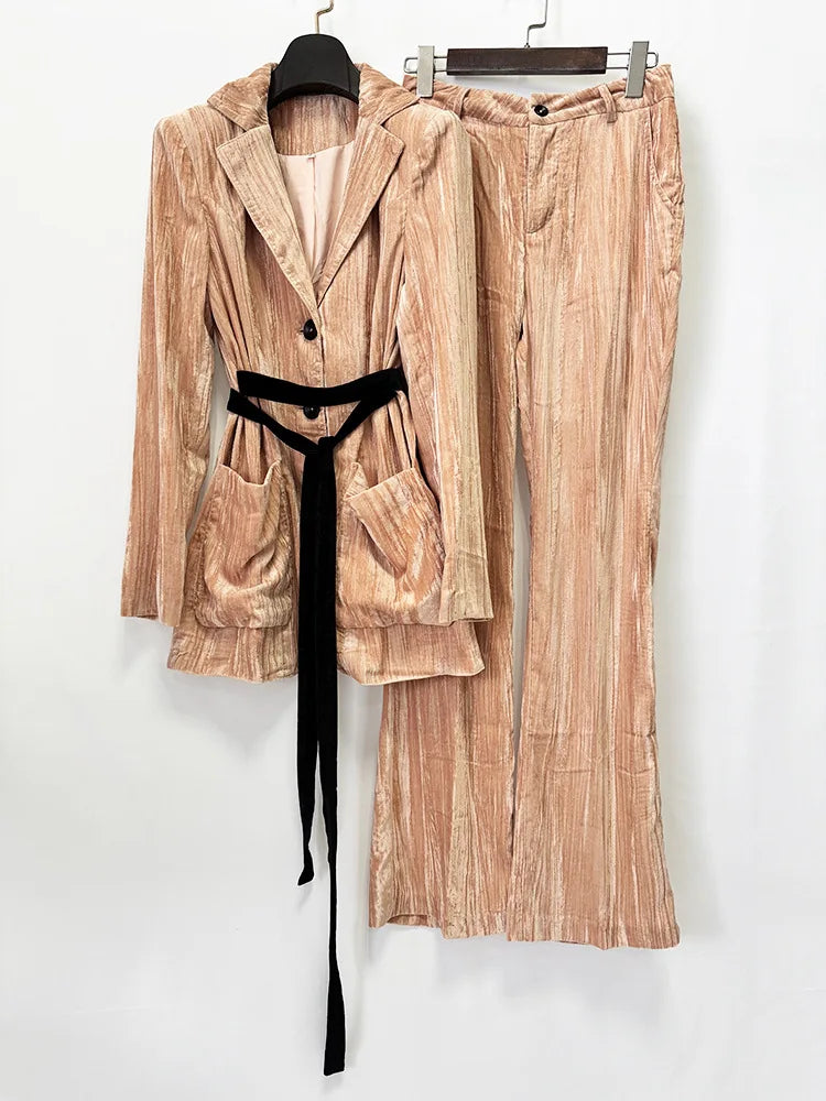 A two-piece women's outfit set featuring a long-sleeve belted blazer and matching wide-leg trousers in a textured, vertically striped peach-beige corduroy-like fabric, styled with a black velvet tie belt, hanging on black hangers against a plain white wall.