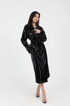 Woman wearing a black glossy trench coat on a white background