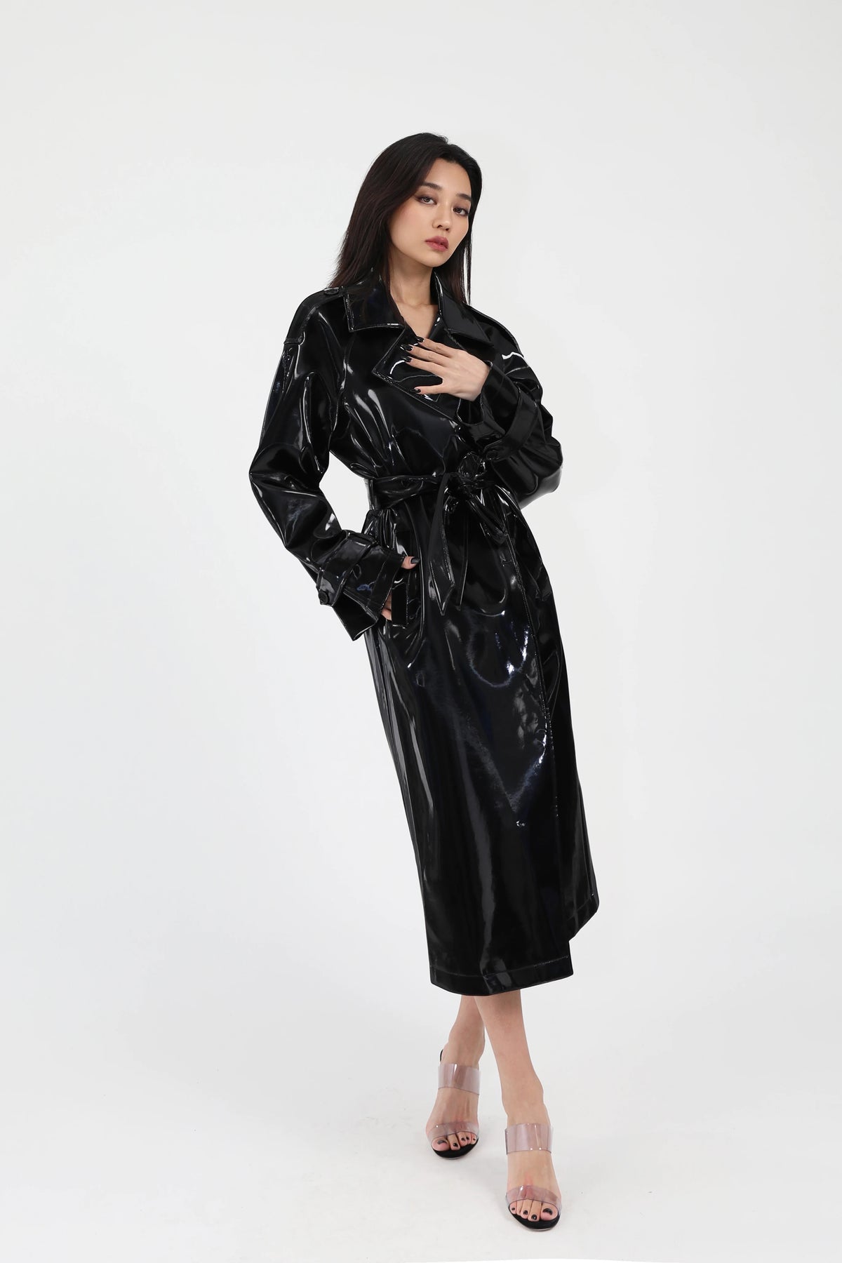 Woman wearing a black glossy trench coat on a white background