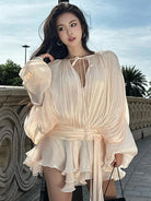 Woman wearing a cream ruched long sleeve mini dress with tie neckline and ruffle hem