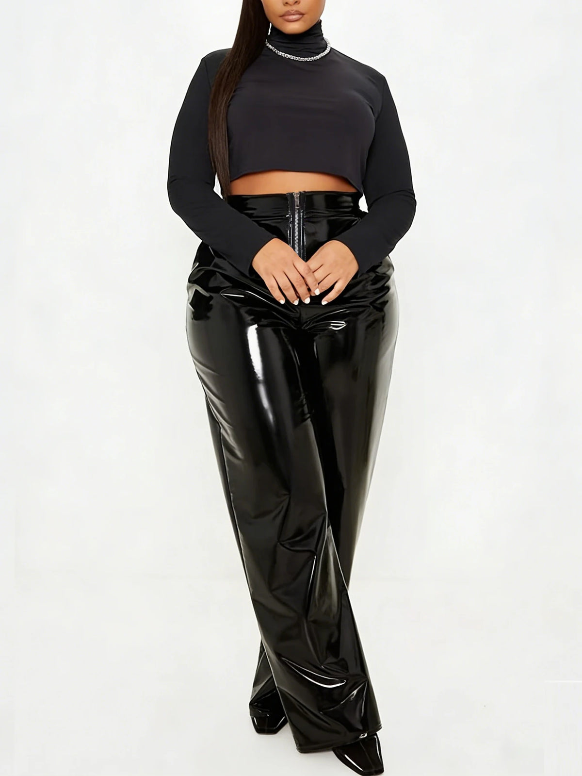 A model wearing a black long-sleeve crop top and high-waisted, wide-leg patent leather pants against a plain white studio background.