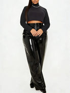 A model wearing a black long-sleeve crop top and high-waisted, wide-leg patent leather pants against a plain white studio background.
