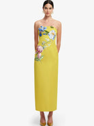 A woman modeling a strapless yellow maxi dress with colorful floral embroidery on the bodice and side.
