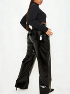 A model wearing shiny black wide-leg patent pants and a black long-sleeve crop top, shown from a side-back angle against a plain white studio background.