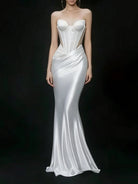 A strapless white satin gown with a structured corset-style bodice, sheer side panels, and a fitted mermaid silhouette, shown on a model against a black studio background.
