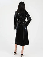A woman viewed from behind wearing a glossy black long coat or wrap with a tie waist, paired with black high heels, against a plain light background.