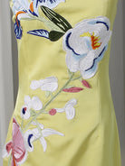 Close-up of a pale yellow dress with large embroidered floral motifs in white, pink, blue, green, and orange.