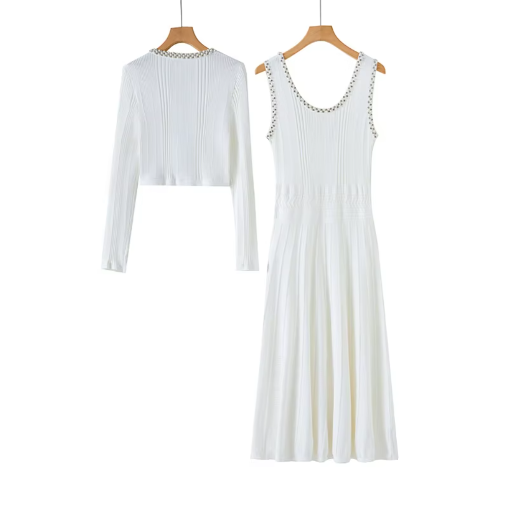A white sleeveless midi dress with a pleated bodice and shoulder chain detailing, shown alongside a matching white long-sleeve cropped knit top on wooden hangers against a white background.